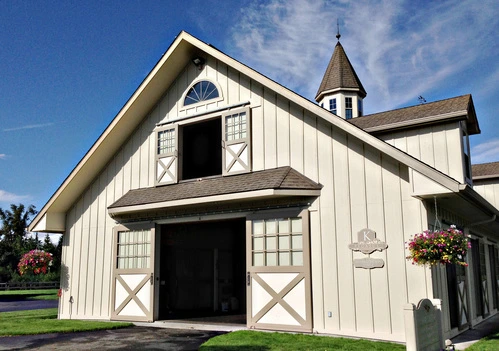 White barn with X-pattern stall doors and arched window in gable