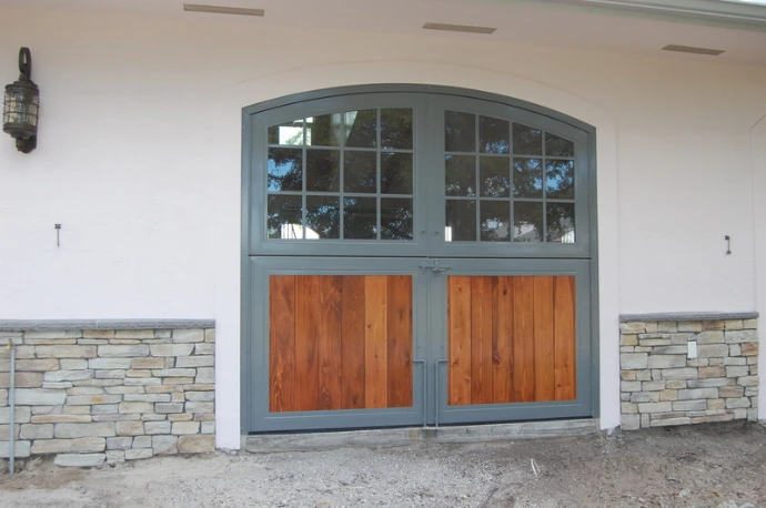 Stucco barn with arched gray metal framed doors featuring wood lower panels and side windows