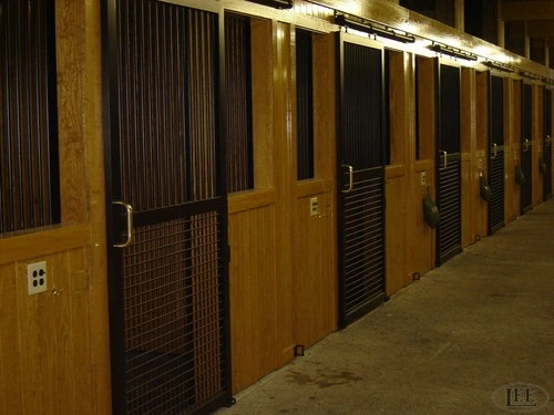 Dark wood barn aisle with vertical slat stall fronts and wire mesh panels in dim lighting