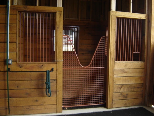 Natural pine stall fronts with wire mesh panels and blue stall guard across opening
