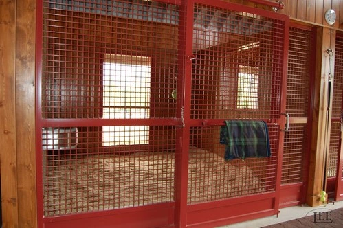 Red metal sliding stall door with wire mesh panel and plaid blanket draped inside
