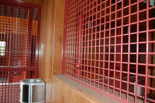 Angled view of red metal stall door with wire mesh panel in natural wood barn interior