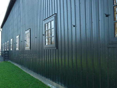 Dark gray-green corrugated metal barn with multiple white-framed barred windows