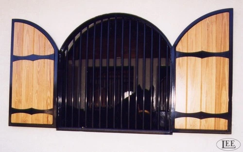 Black arched center window with natural wood panel shutters hinged open on cream stucco wall