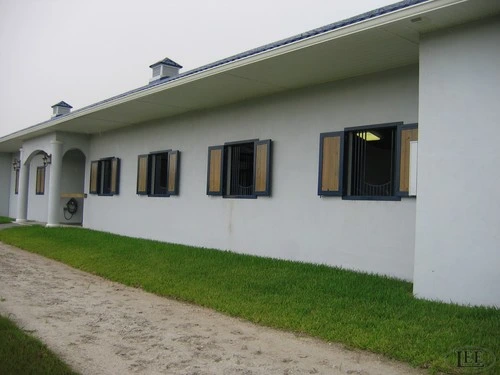 White stucco European-style building with black louvered shutters on multiple windows