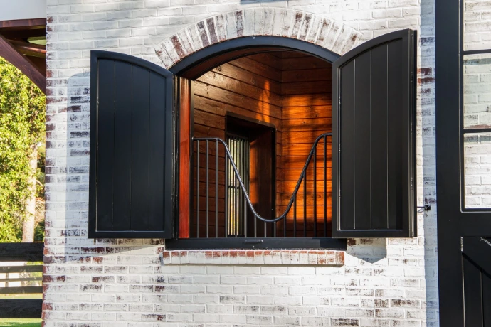 Black metal arched shutters opened to reveal brick archway with warm wood interior and vertical bar grills