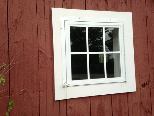 Red board-and-batten barn wall with white six-pane window flanked by red shutters