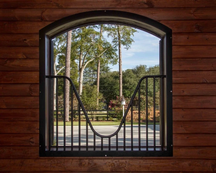 Black metal arched window grill with decorative curved bars on dark wood wall