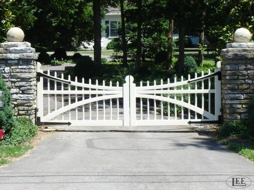 White curved double gates with vertical pickets between stacked stone pillars with decorative sphere caps