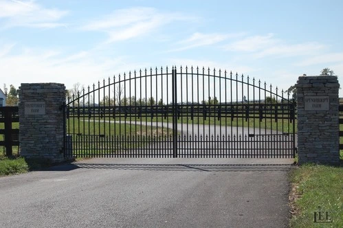 Black metal arched gate between dark stone pillars on asphalt entrance drive