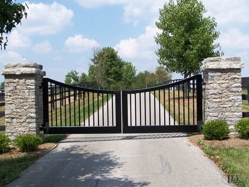 Black metal double gates with arched curved design between stacked stone pillars on paved driveway