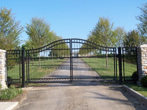 Black metal double gates with arched tops and circular decorative elements between stacked stone pillars