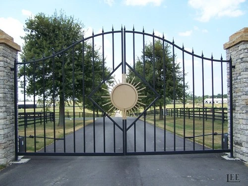 Black metal double gates featuring circular medallions and arched design between stone pillars on paved drive