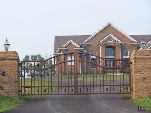 Brown ornamental metal gates with decorative scrollwork between brick pillars in front of brick mansion