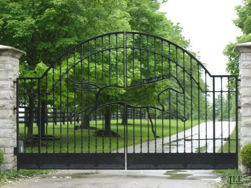 Black ornamental double gates with arched tops and grid design between stone pillars with lush greenery