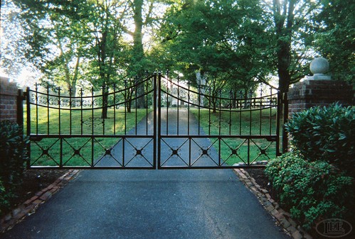 Black metal gate featuring decorative X-pattern crossbars and curved arch top on driveway