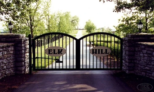 Black ornamental double gates with arched tops and custom name plaques mounted on brick pillars