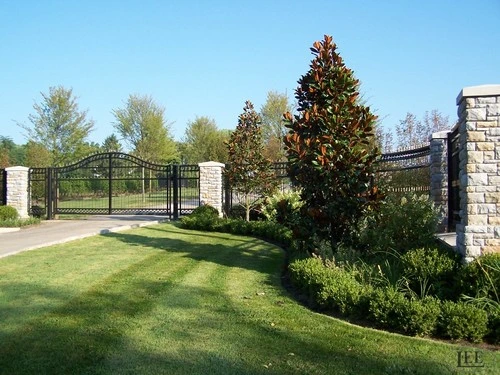 Black ornamental double gates between stone pillars with professional landscaping and seasonal decorative tree