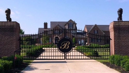 Black ornamental gates with decorative monogram medallion between brick pillars topped with lion statues