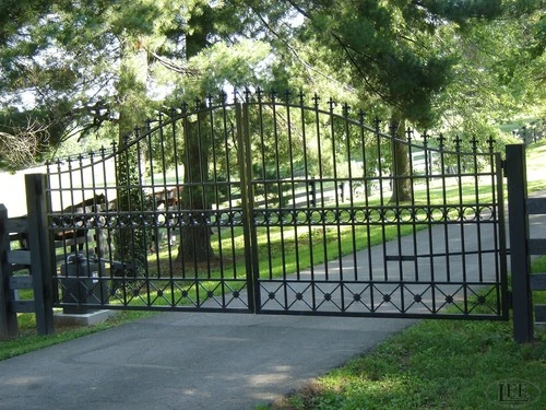 Black ornamental metal double gates with decorative scrollwork and curved arch tops on paved driveway