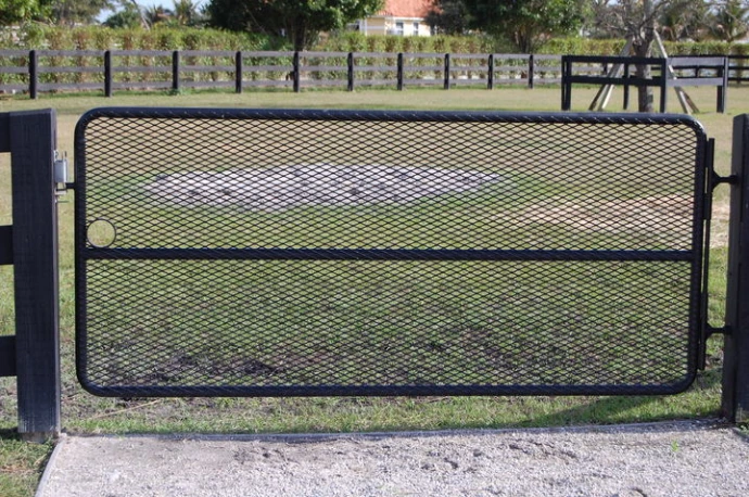 Black metal paddock gate with expanded mesh panel centered between dark fence posts