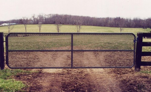 Black metal tube gate with three horizontal rails spanning pasture opening