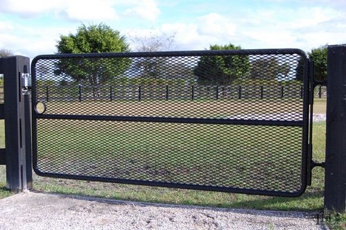 Black metal mesh panel gate in open position with green pasture and mature tree visible