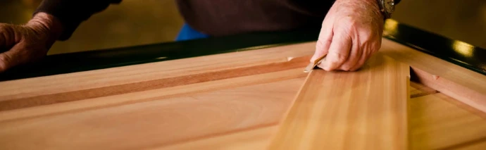 Close-up of hand applying stain or finish to natural wood board surface with brush