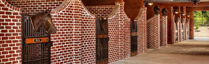 Red brick interior barn corner showing arched stall openings with dark shadows and textured masonry walls