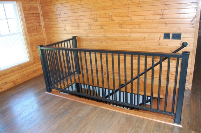 Black metal vertical bar interior stair railing on upper level overlooking natural wood floor with vaulted ceiling and skylight