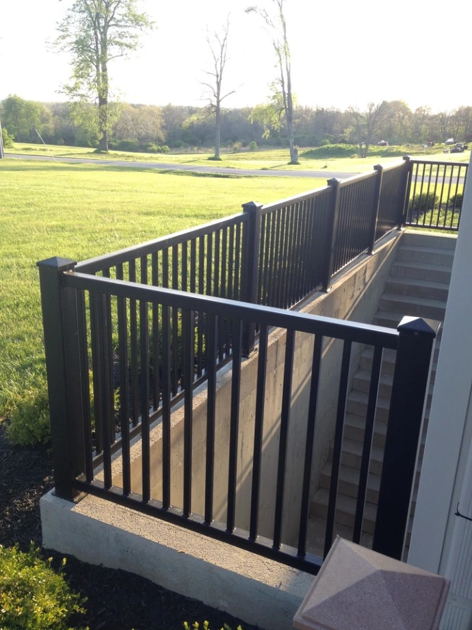 Close-up angled view of black aluminum vertical picket deck railing with horizontal top rail against green pasture background
