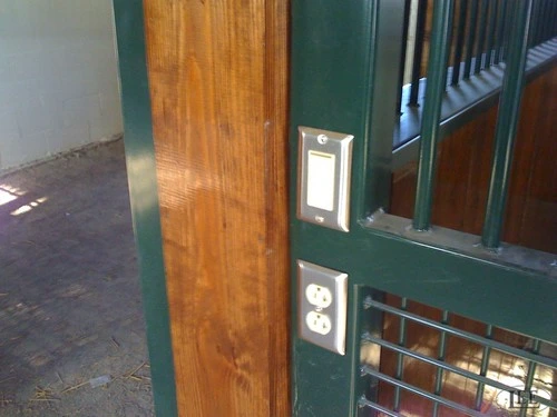 Dark green stall front panel with mahogany lower section and electrical outlet on natural wood wall
