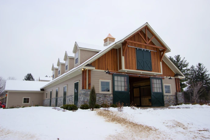 Natural wood barn with timber-frame gable and X-pattern double doors under peaked roof in winter with snow