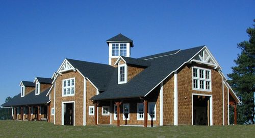 Tan barn with dark roof, white cupola and multiple dormer windows along roofline