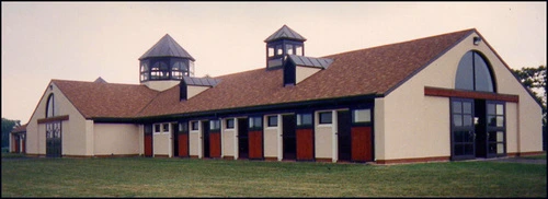 Cream barn with burgundy roof trim, cupolas and multiple X-pattern stall doors along front