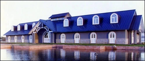 European-style barn with mansard blue roof, dormers and cream colored stucco walls along waterfront