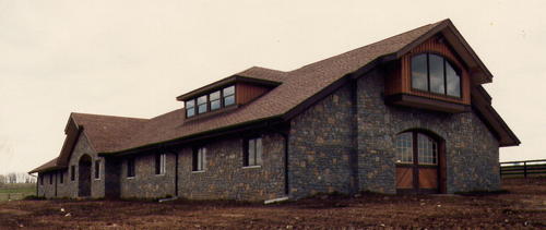 Stone barn exterior showing multiple levels with varied brown roof sections and window placements