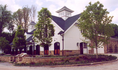 White barn with cupola, covered porch and stone terraced landscaping with mature trees