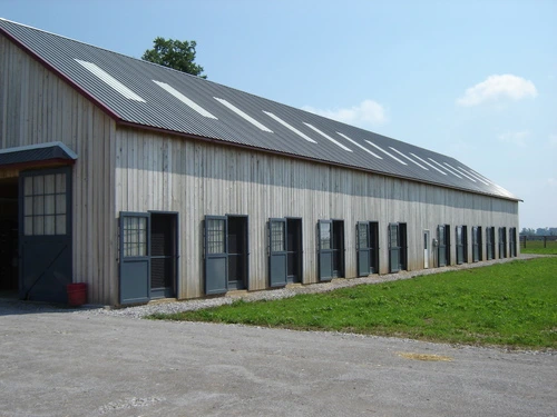 Gray metal barn with white skylights, multiple stall openings along length