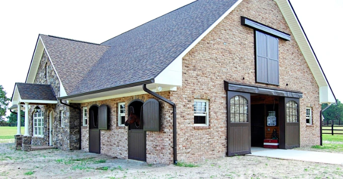 Tan brick barn with dark roof, white trim and stone pillars under construction