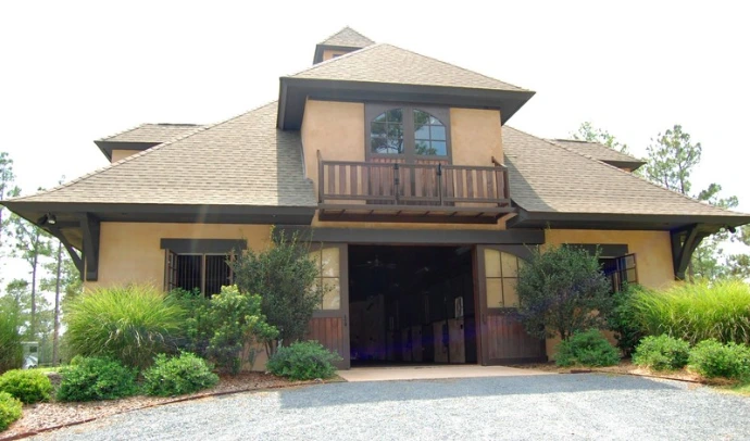 Tan stucco barn with brown trim, cupola and landscaped entrance with curved driveway