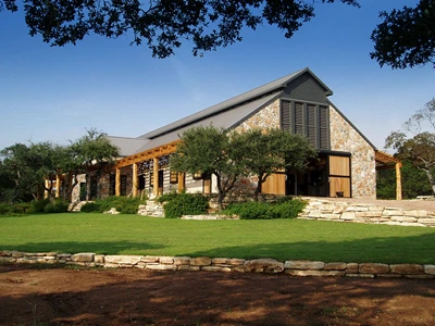 Stone and stucco barn with timber-frame details, pergola and landscaped lawn setting