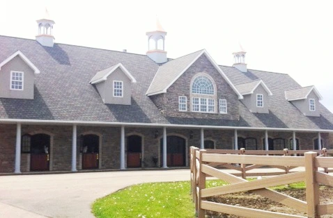 White barn with dark roof, multiple cupolas and covered front porch with white fencing