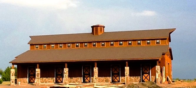 Tan barn with burgundy roof trim and X-pattern stall doors along front elevation