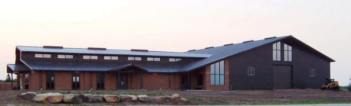 Red brick barn with dark roof visible at dusk with interior lighting