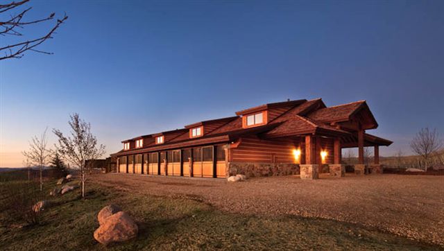 Long brown barn with illuminated stall openings at dusk on hillside setting
