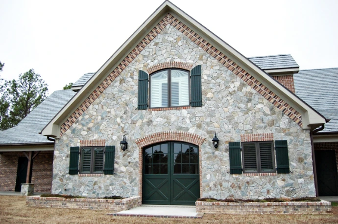 Stone barn with decorative brickwork, green shutters and arched entrance gable
