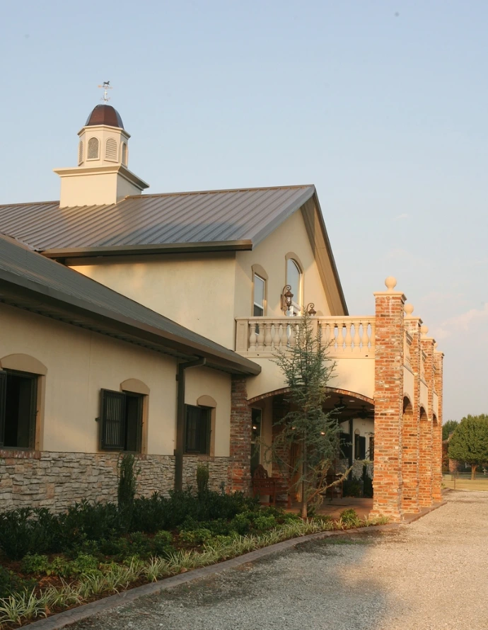 Cream stucco barn with green roof, arched openings and red brick chimney