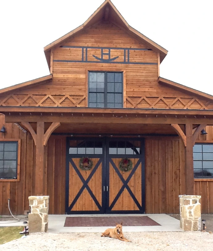 Natural cedar barn with timber-frame overhang showing X-pattern doors and multi-pane windows