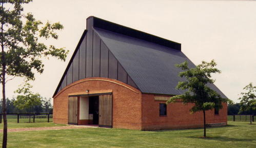 Modern red brick barn with dark metal roof and large glass panel openings on green pasture